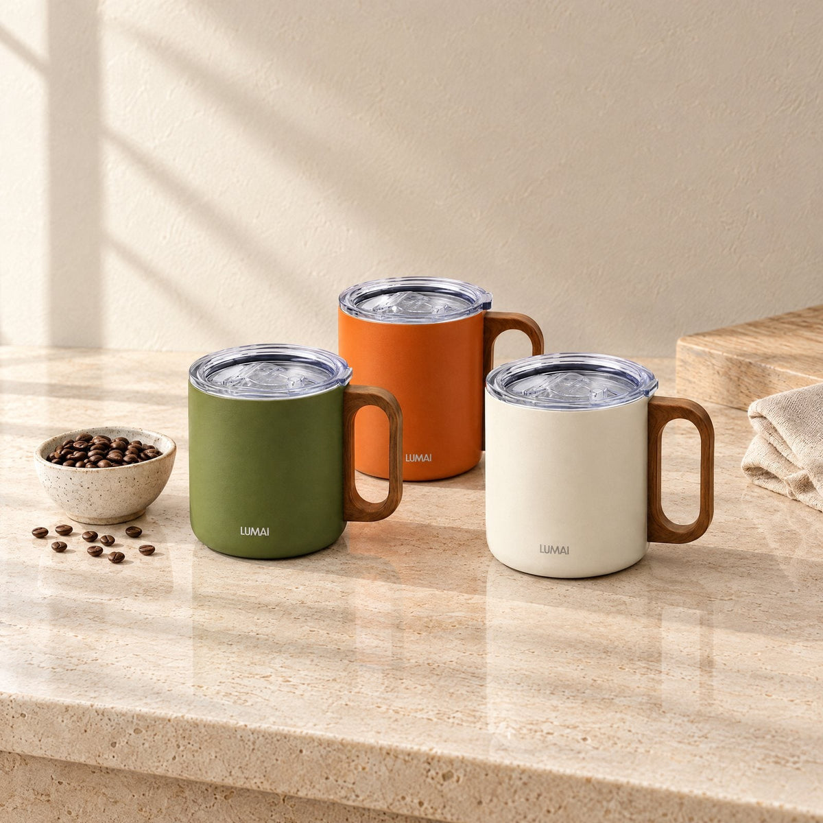Canecas Caraíva verde, laranja e branca, com tampa, sobre uma bancada de pedra clara com grãos de café (ambiente ilustrativo)