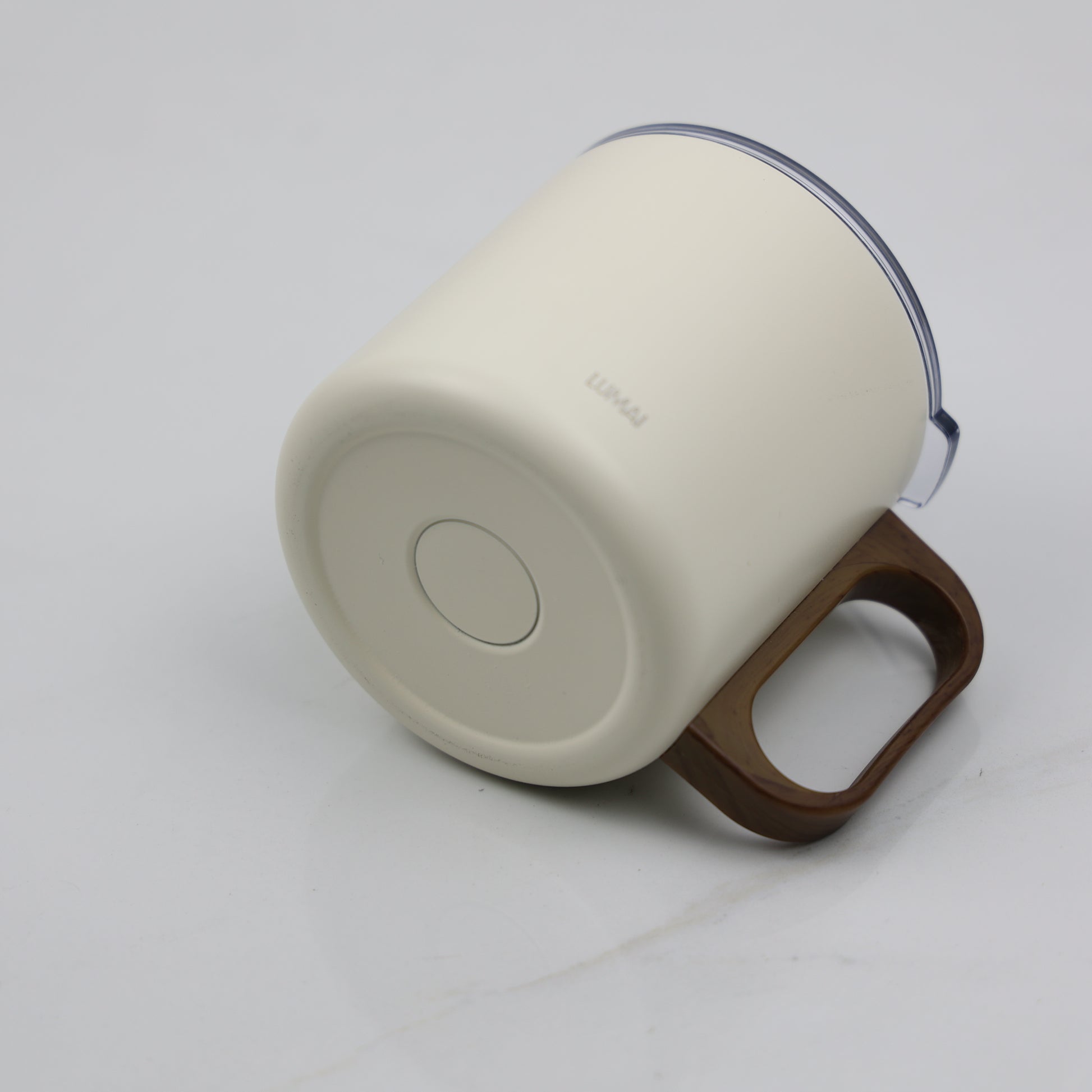 Ângulo inferior da caneca mostrando base circular branca com logo Lumai e alça arredondada em tom amadeirado