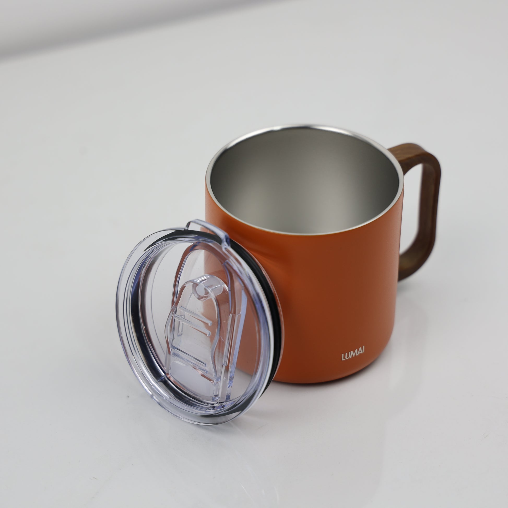 Caneca térmica laranja aberta com tampa transparente ao lado, mostrando interior em aço inox