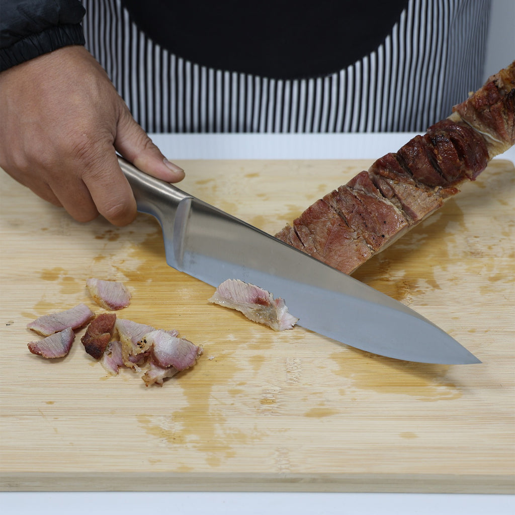 Faca de lâmina larga em aço inox fatiando carne assada sobre tábua de madeira clara