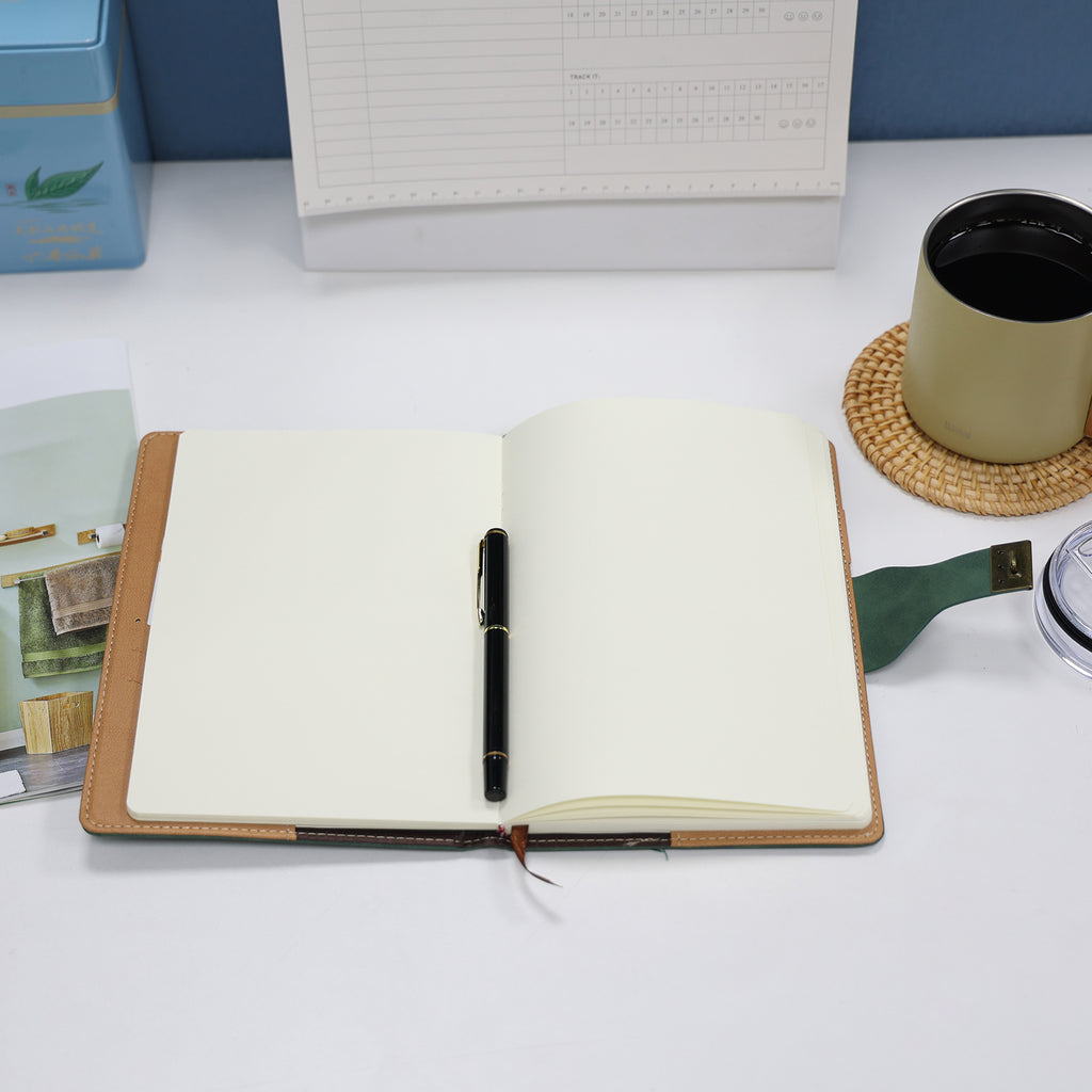 Foto do Caderno com Cadeado Cartagena LUMAI verde aberto, mostrando páginas internas em branco com caneta, sobre mesa em ambiente de escritório.