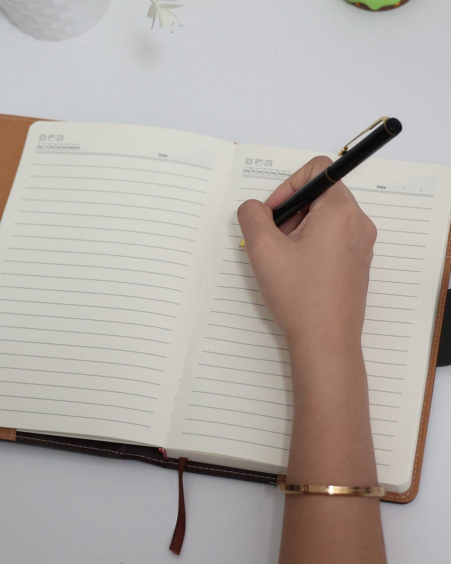 Caderno LUMAI Cartagena chumbo aberto com a mão escrevendo uma lista